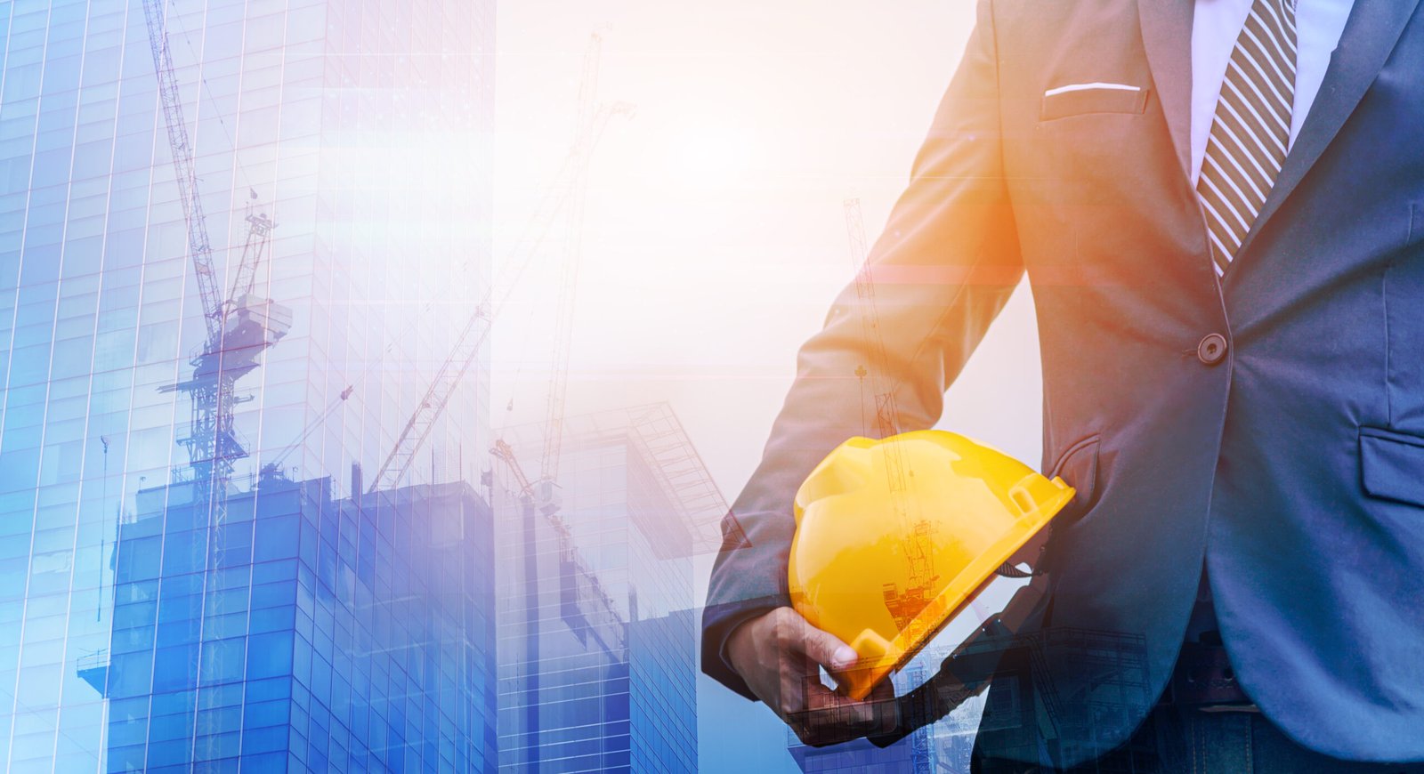 Double Exposure of building under construction and man engineer is holding helmet wearing a suit thinking of ways and ideas for building new buildings in the future.